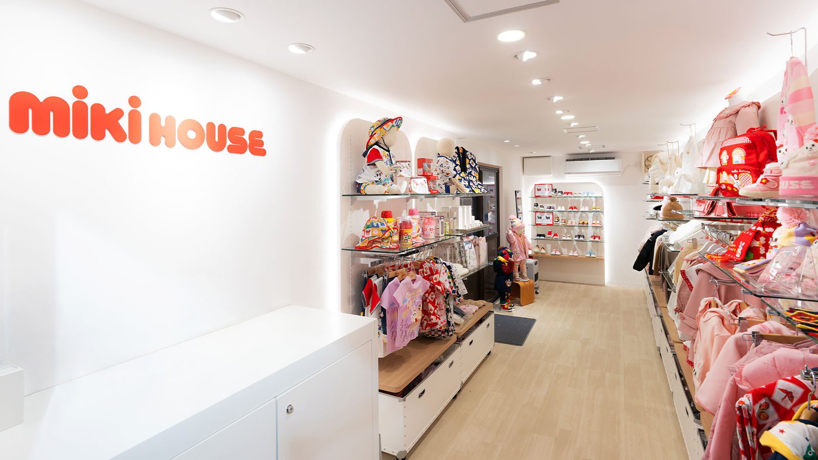 店内の通路。左に白いカウンターと赤いロゴの壁、両側にガラス棚の什器が奥まで続く