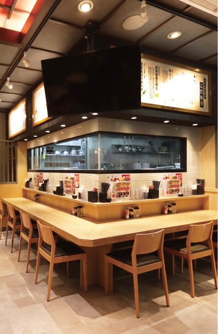ちゃんぽん亭 草津駅前店の内装（滋賀県・麺の店・L字の木のカウンターと木の椅子、ガラス越しに見える厨房）