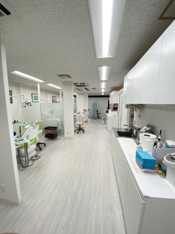 多摩市のクリニック（東京都多摩市）の診療室。すりガラス調の仕切りで区切った歯科ユニットの列と、向かいの通路沿いにシンク付きの白いカウンターと収納（株式会社S plus Design’s）