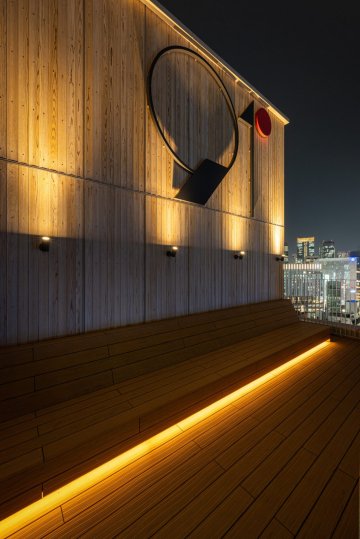 91°SAUNA 東京都 サウナ 木×間接照明・サウナ室の段床 屋上の外気浴スペース。木のベンチと夜景（サンリット建設（DESIGN STUDIO TEMPO））
