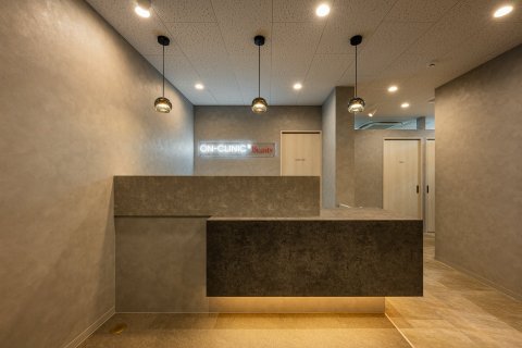 ON-CLINIC 東京都 美容クリニック モルタル調×間接照明・ミニマル 受付。モルタル調の壁とカウンター、ペンダント照明(サンリット建設(DESIGN STUDIO TEMPO))