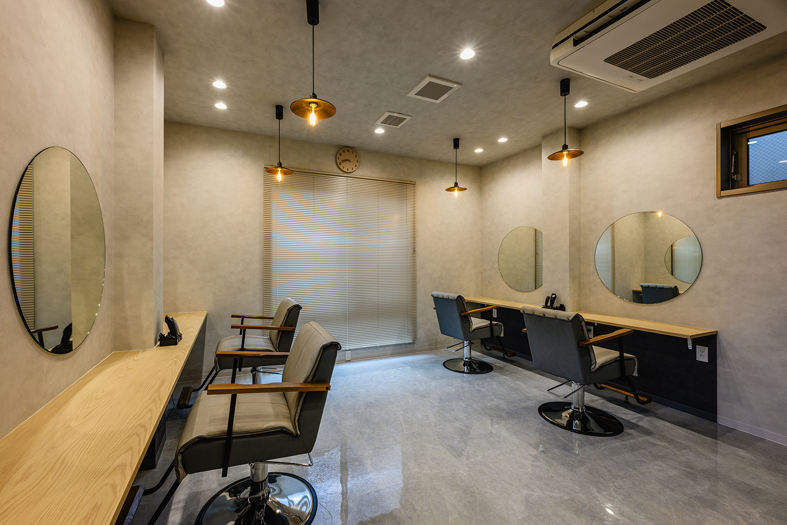 美容室の施工写真:hair salon Relish(東京都)のカットスペース全景──丸鏡4面と木の造作カウンター、ペンダント照明、壁掛け空調 施工:株式会社サンリット建設