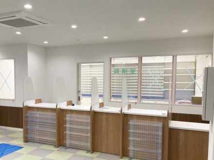 あいり薬局（東京都足立区）の投薬カウンター。白い仕切り板で分けた窓口と右端の低い天板、奥に「調剤室」と書いたガラス窓と薬棚（施工：株式会社ビリーフデザイン）
