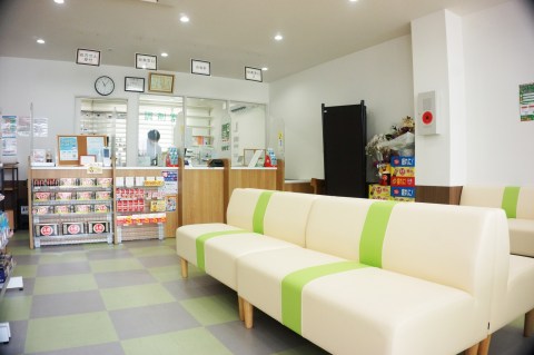 あいり薬局（東京都足立区）の待合。緑のラインのソファと市松の床、奥に「調剤室」と書いたガラス窓の受付カウンター（施工：株式会社ビリーフデザイン）