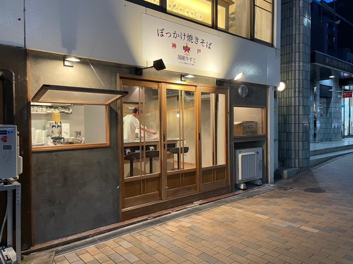 ぼっかけ焼きそば専門店 神戸市中央区 夜の外観。木製の引き戸とテイクアウト窓、モルタル仕上げの外壁、白い看板とスポットライト（LEBON DESIGN）