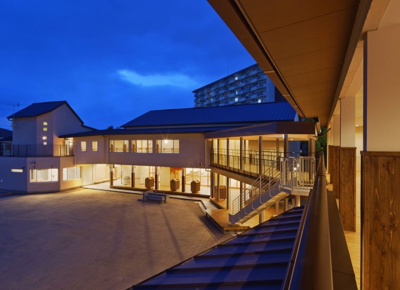 向島幼稚園の外観（夕景）。2階建ての園舎と園庭、テラスと外階段（クサノユカリ建築設計室 公式サイト掲載・代表が住建設計在籍時に担当）