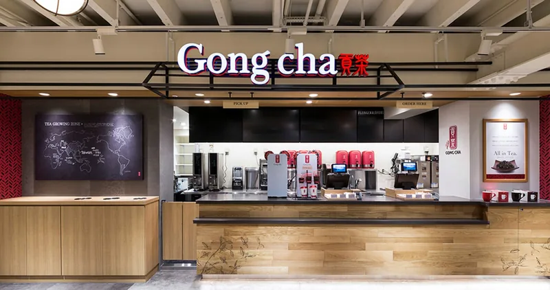 ゴンチャの店舗のカウンター。赤いロゴのサインの下に、木のカウンターとドリンクの機器、壁の写真パネル（株式会社ノムラアークス）