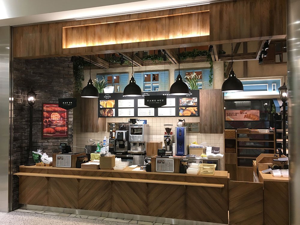 木目の腰壁とカウンター、コーヒーマシンとペンダント照明のカフェ