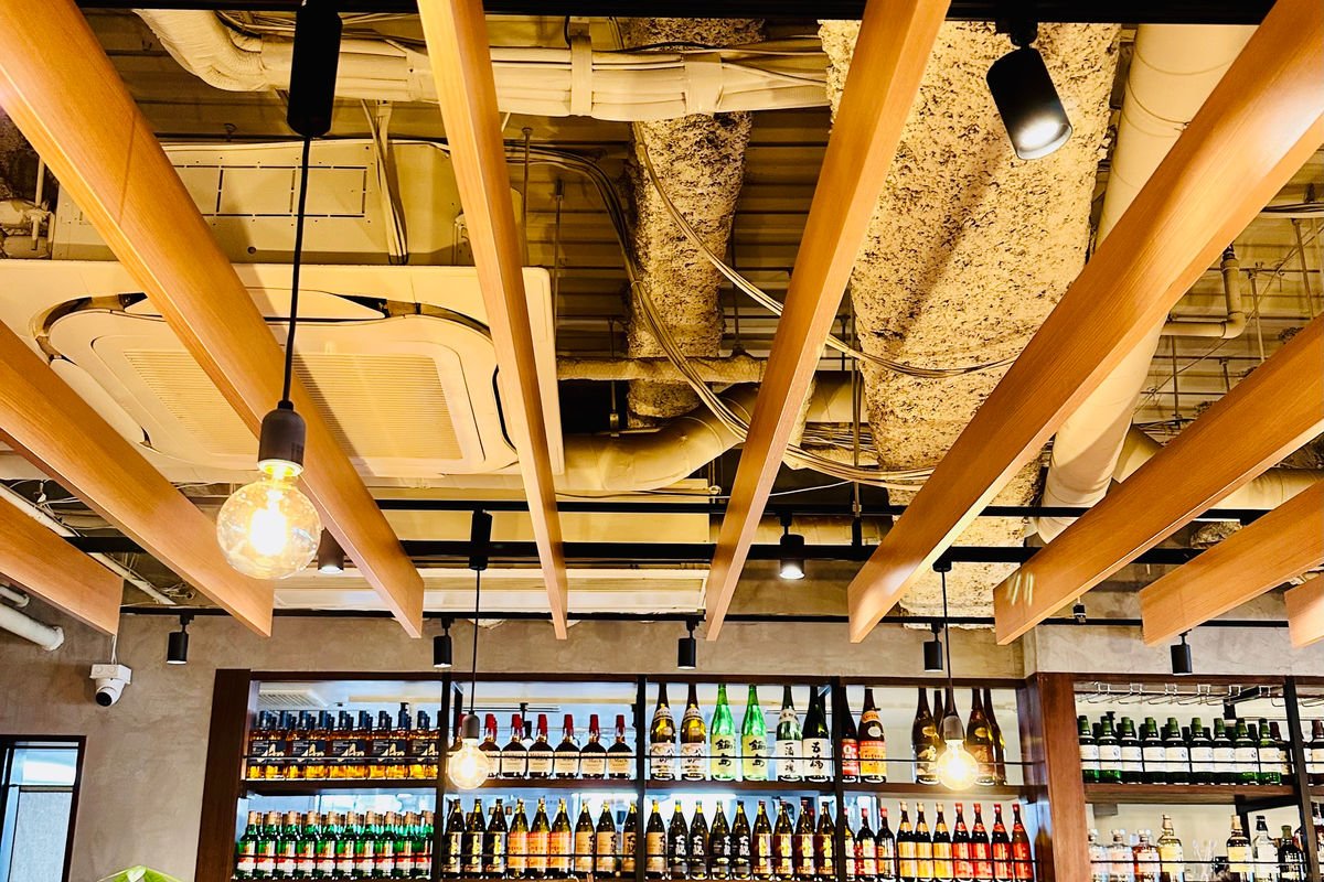 木の梁と配管を見せた天井、酒瓶の棚の中華居酒屋