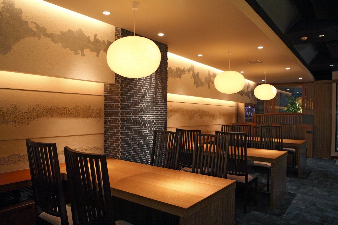 木のテーブルと椅子、雲のような和紙の照明、壁の絵の和食店の客席