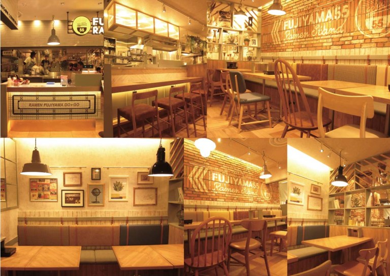 FUJIYAMA55 RAMEN STAND 名古屋パルコ店：ロゴを描いたれんがの壁、木の椅子とテーブル、つり下げの照明、額を並べた明るい客席