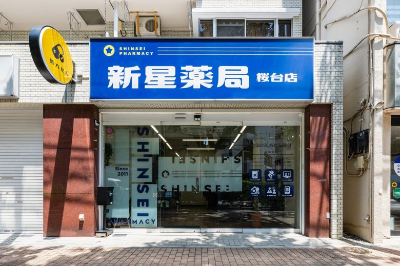 新星薬局 桜台店（東京都練馬区）の外観。青い看板「新星薬局 桜台店」、黄色い丸い「処方せん」の袖看板、ガラスの自動扉（施工：株式会社サンリット建設）