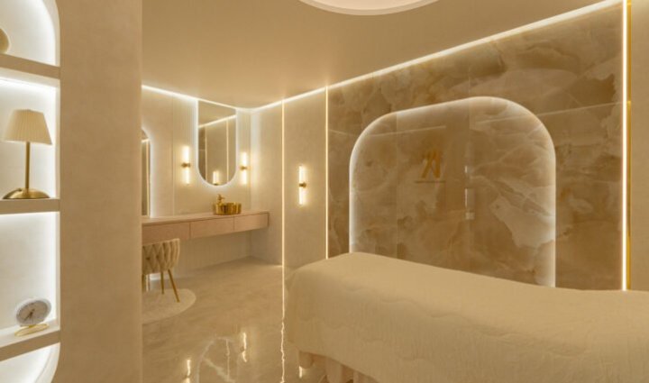 beauty salon ELEVENの施術スペース。大理石調の壁と輪郭に沿った照明、棚、施術ベッド、光沢のある床（株式会社colmo design plus i）