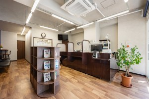 木の床に受付カウンターと雑誌ラックを置いた調剤薬局の待合（新星薬局桜台店・サンリット建設）