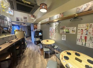 壁にメニューを貼り丸いテーブルを置いた大衆居酒屋の店内（ネオ大衆 カモメヤ 小岩・タカハシアートプランニング）