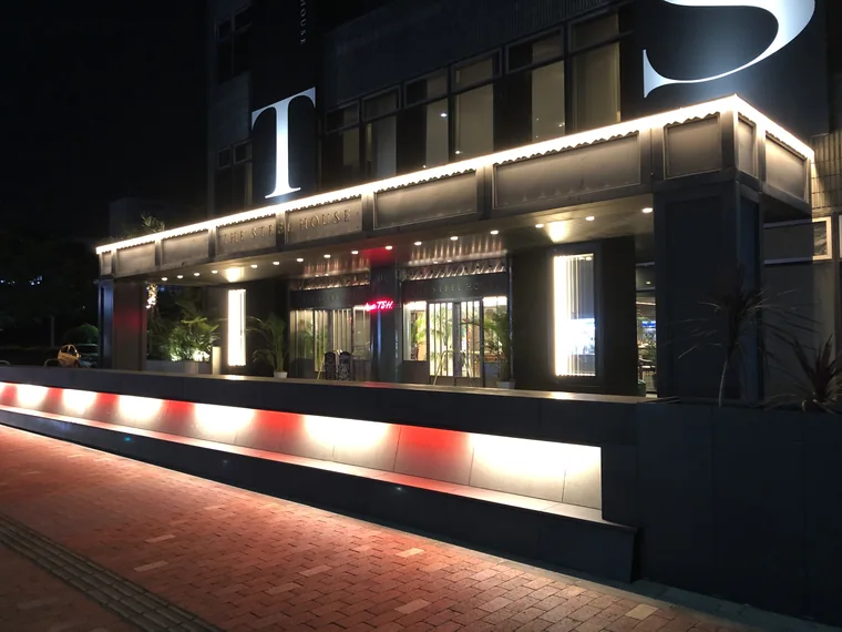 建物名を掲げた庇の下を照らし、ガラス扉へとつなぐ夜のエントランス。
