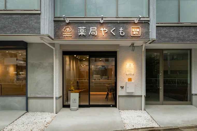 薬局名のサインを入口の上に設けています。ガラス越しに待合と店内の照明が見えます。