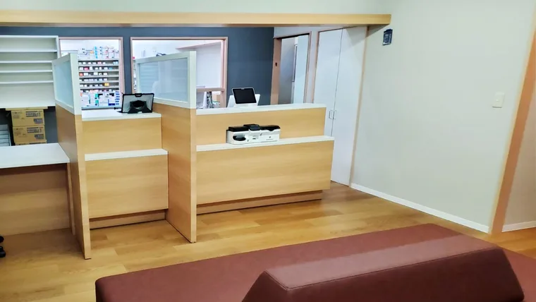 隣の窓口と仕切りで区切ったカウンターを配置しています。手前には待合のソファがあり、背面には薬品棚が見えます。