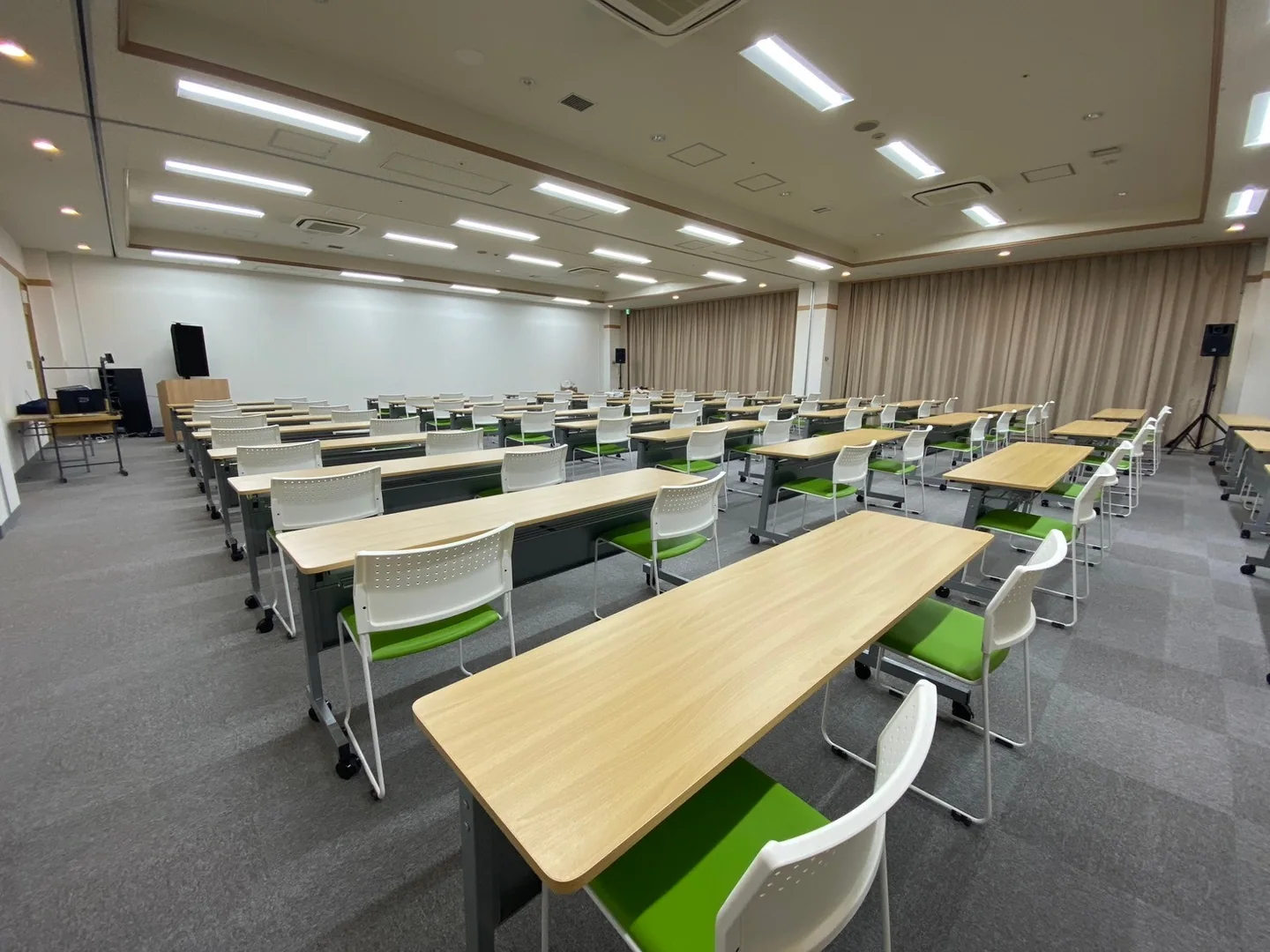 技術技能講習センター株式会社の講習会場です。長机と緑の座面の椅子を並べ、列の周りに通路を設けています。