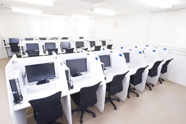 一人ずつ区切った学習席に、パソコンとヘッドホンを設置しています。列の横に通路を設けた予備校の教室です。