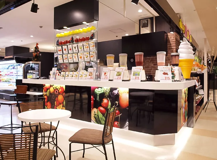 ジュース等を扱う複合店の事例です。白いカウンターにメニューと商品サンプルを並べ、手前にはテーブルと椅子を配置しています。